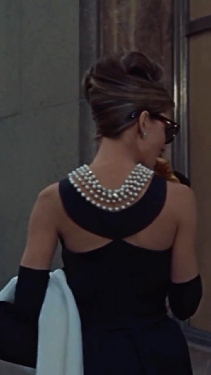 Woman in black dress and pearls with an elegant updo hairstyle from behind.