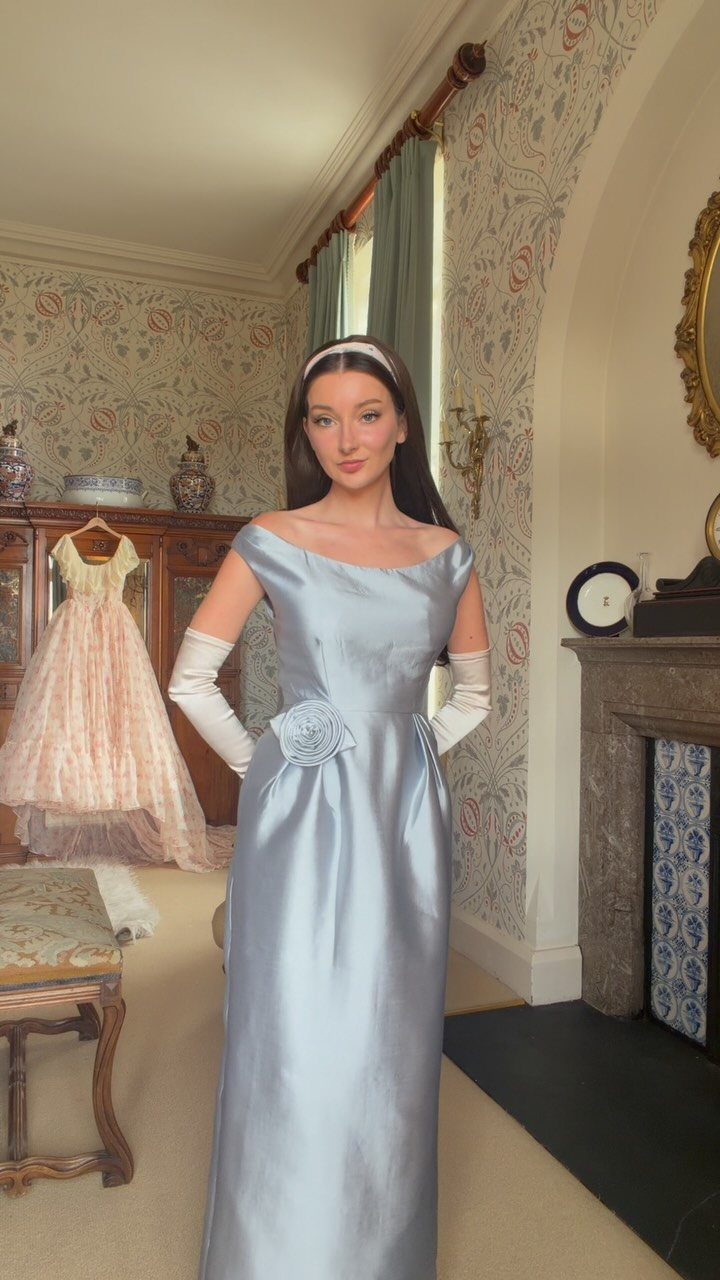 Woman in a light blue satin gown and white opera gloves in vintage room