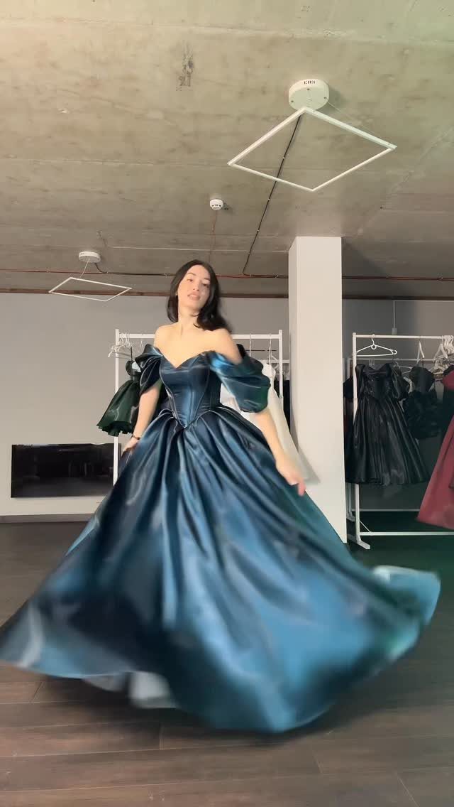 Woman in a voluminous teal satin off-the-shoulder ballgown posing in a studio.