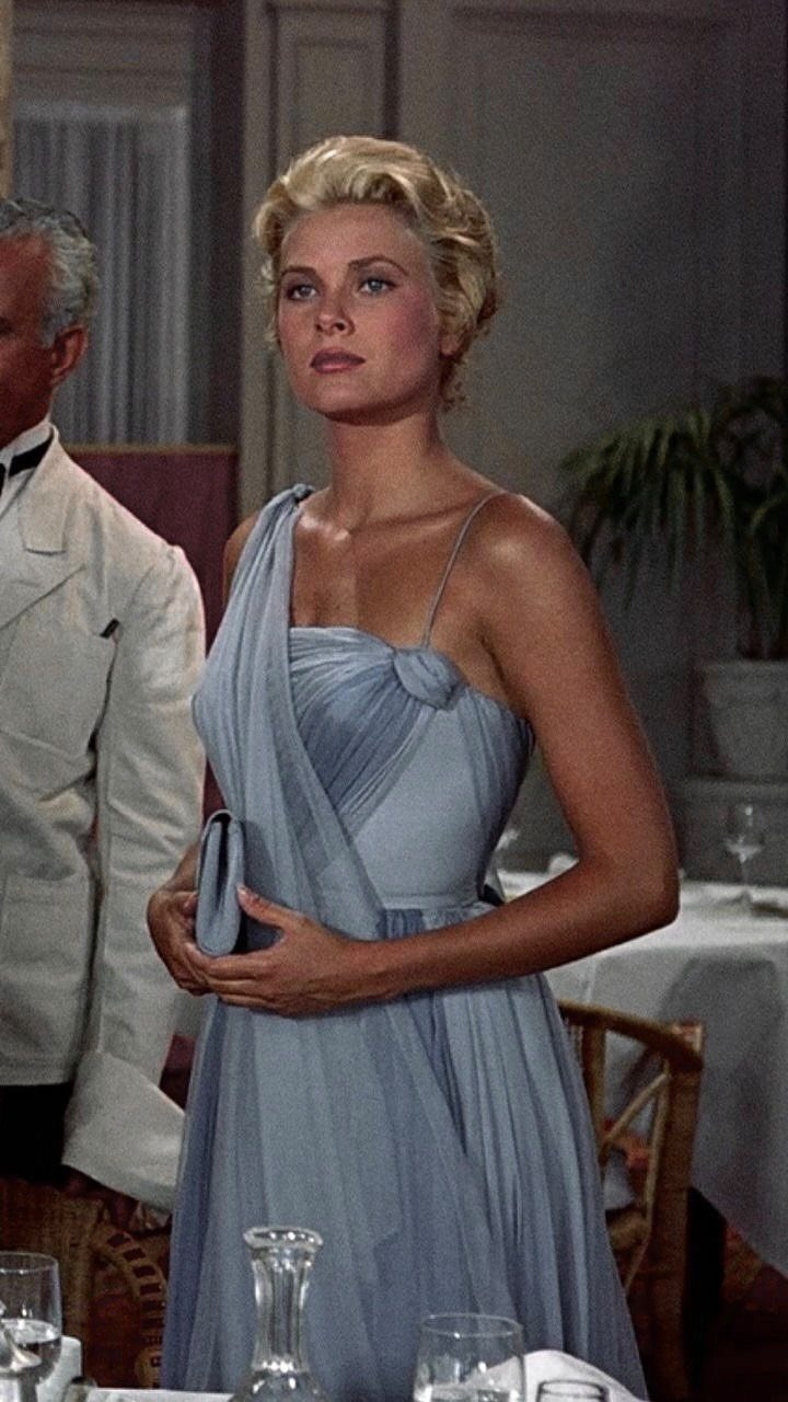 Woman in a light blue one-shoulder draped gown in a formal dining setting.