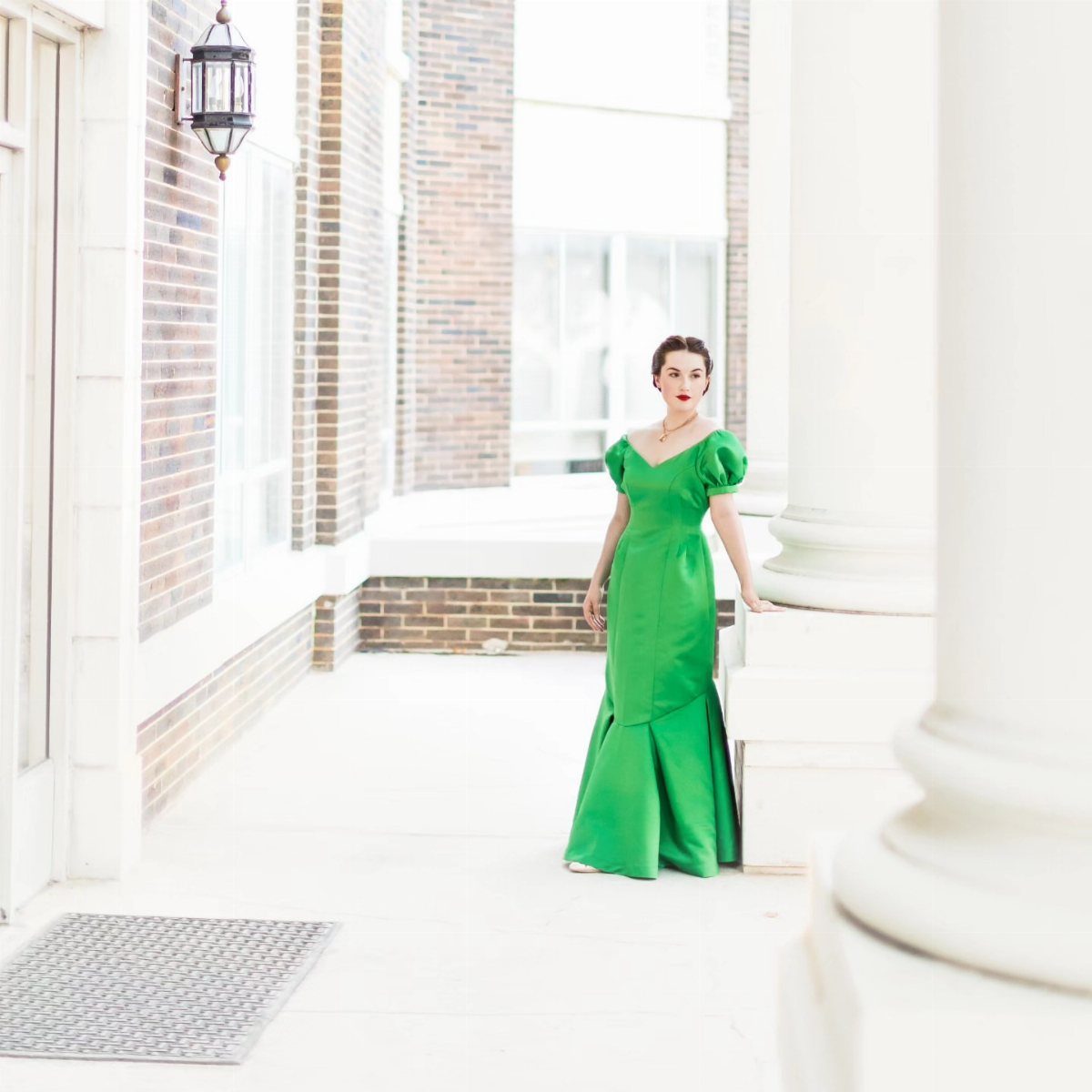 Woman in a bright green satin gown with puffed sleeves standing by white columns.