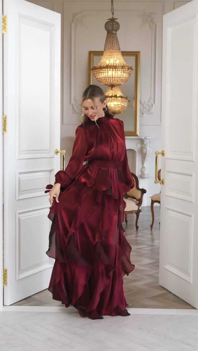 Woman in a burgundy ruffled silk gown standing in a white doorway.