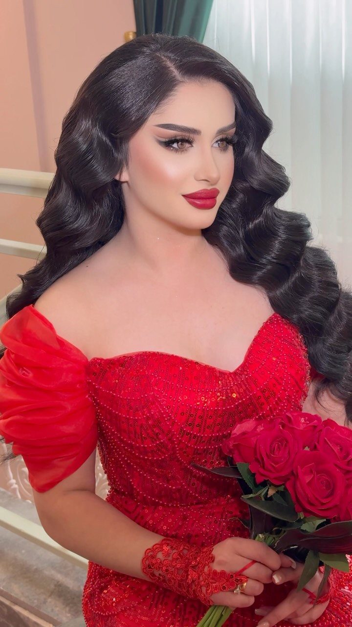Woman in a sparkling red off-the-shoulder gown holding a bouquet of red roses.