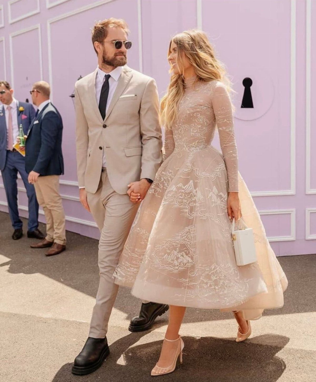 Woman in a champagne tea-length lace gown walking with a man in beige suit.
