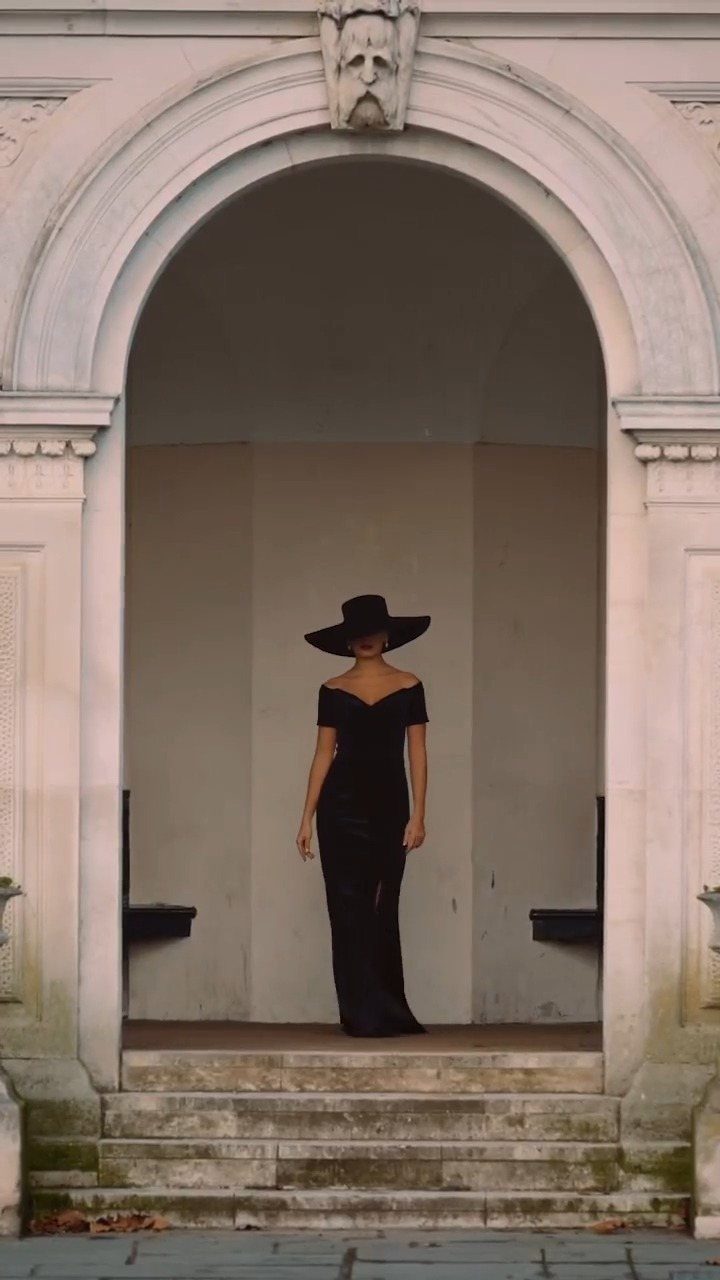 Woman in a long black gown and wide-brimmed hat standing in a stone archway