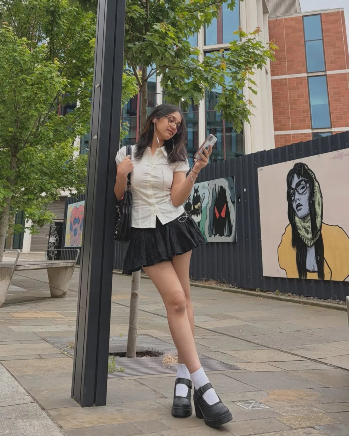 Woman wearing a white button-down shirt and black pleated mini skirt with chunky loafers.