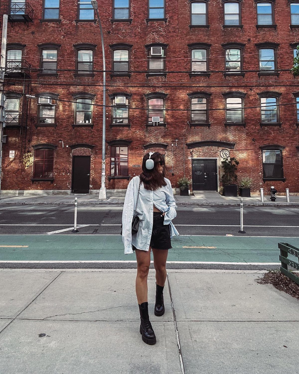 Woman in a black mini skirt and ankle boots standing on a city sidewalk.