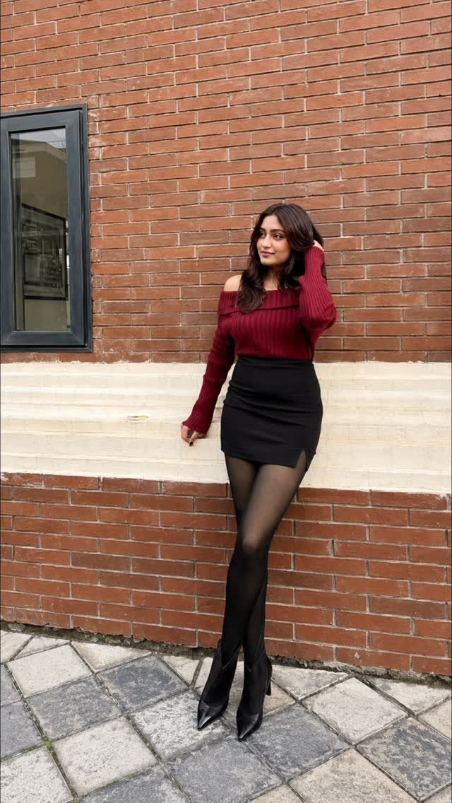Woman wearing a maroon top and short black skirt with black tights and heels.