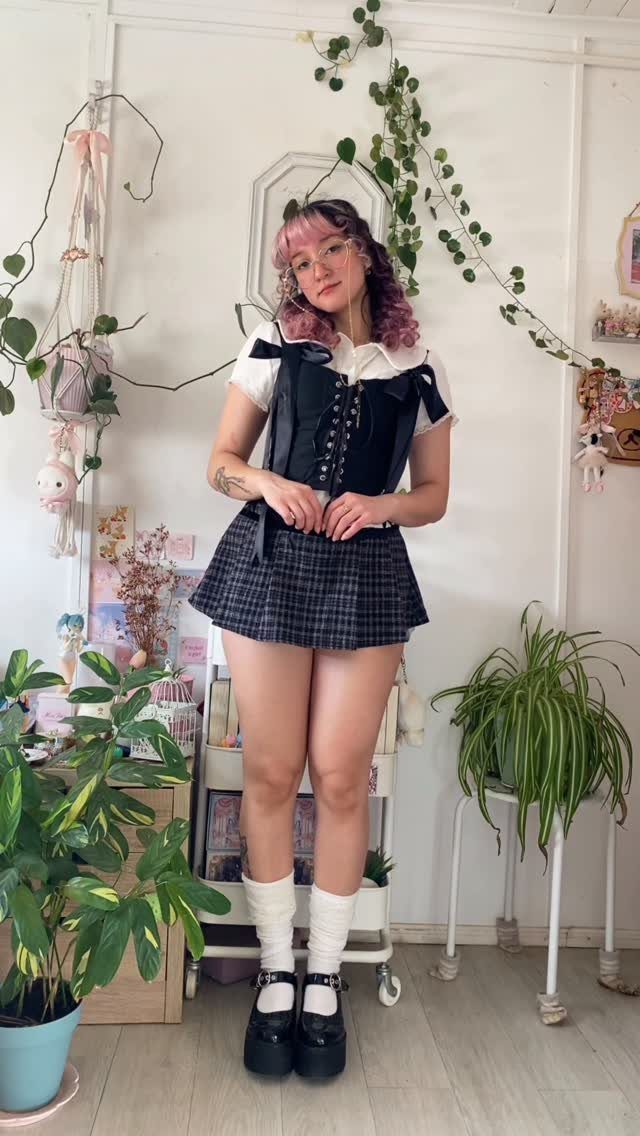 Woman wearing a black corset and short plaid skirt with platform shoes.