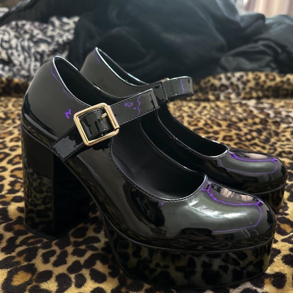 Black patent leather platform heels with gold buckles on leopard print fabric.