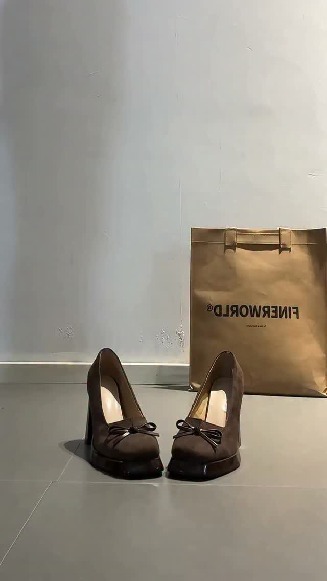 Brown platform high heels with bows sitting next to a brown shopping bag.