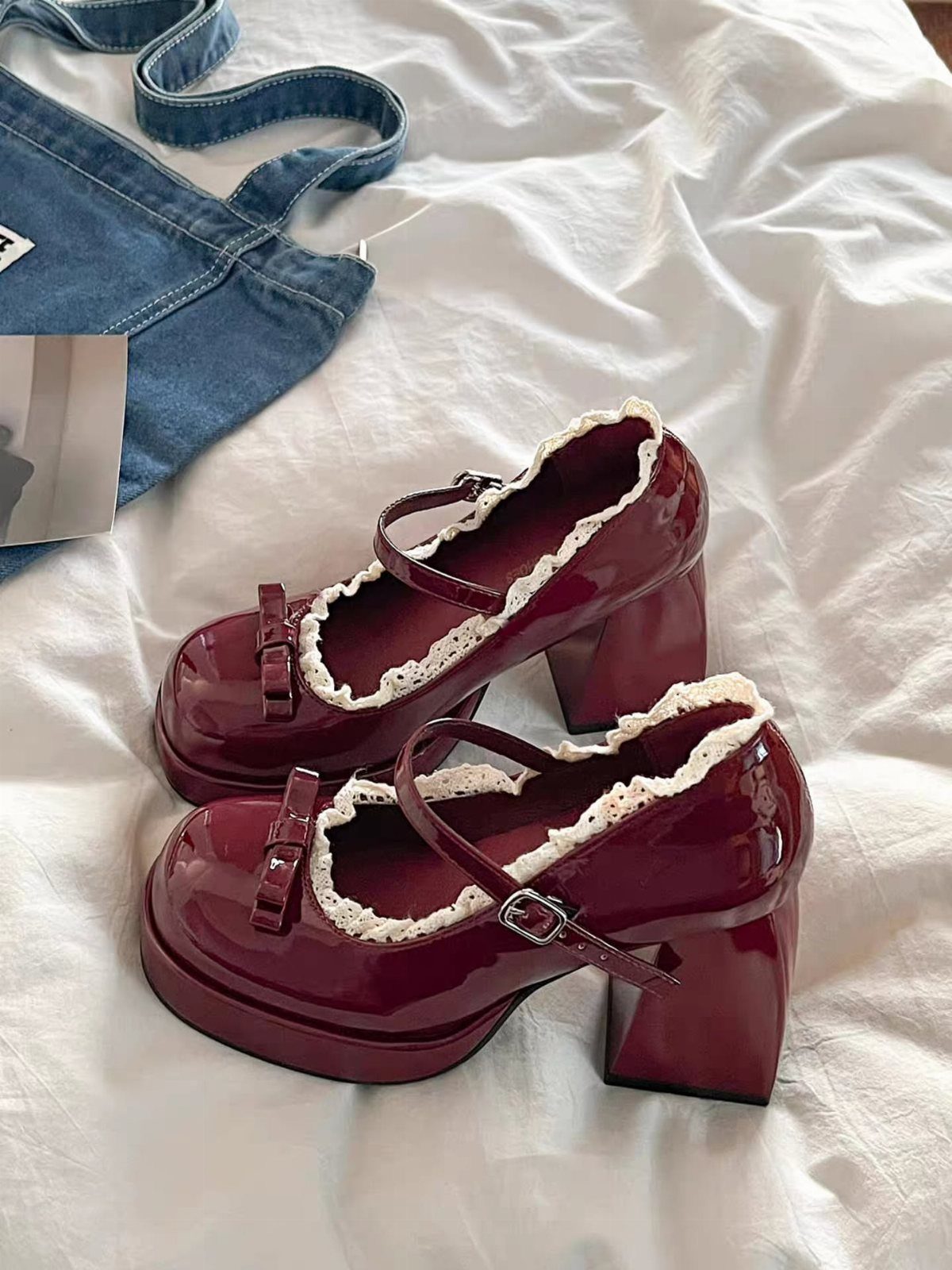 Burgundy patent leather platform heels with white lace trim on white fabric.