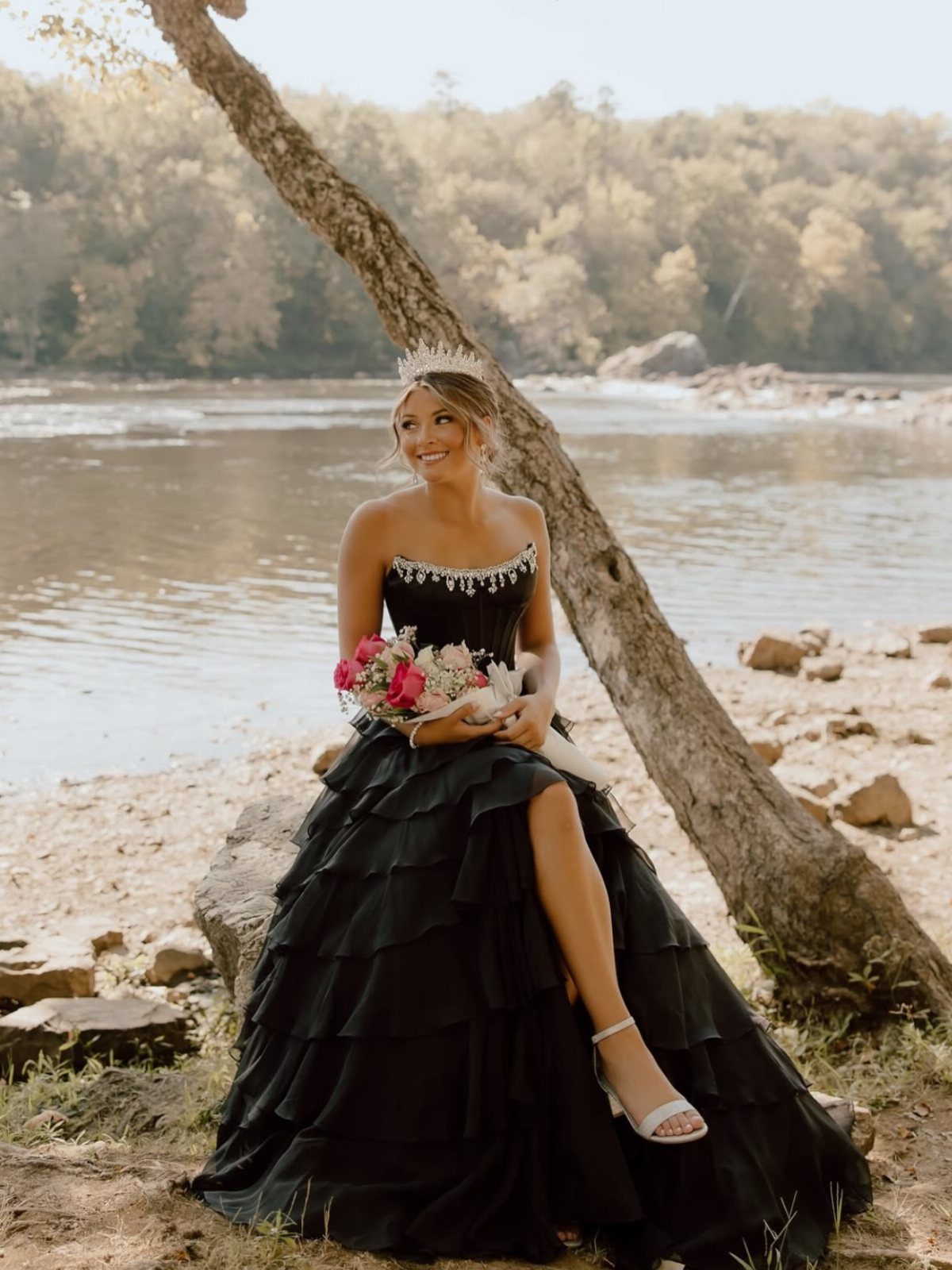 Woman in a black tiered ball gown and tiara sitting by a river
