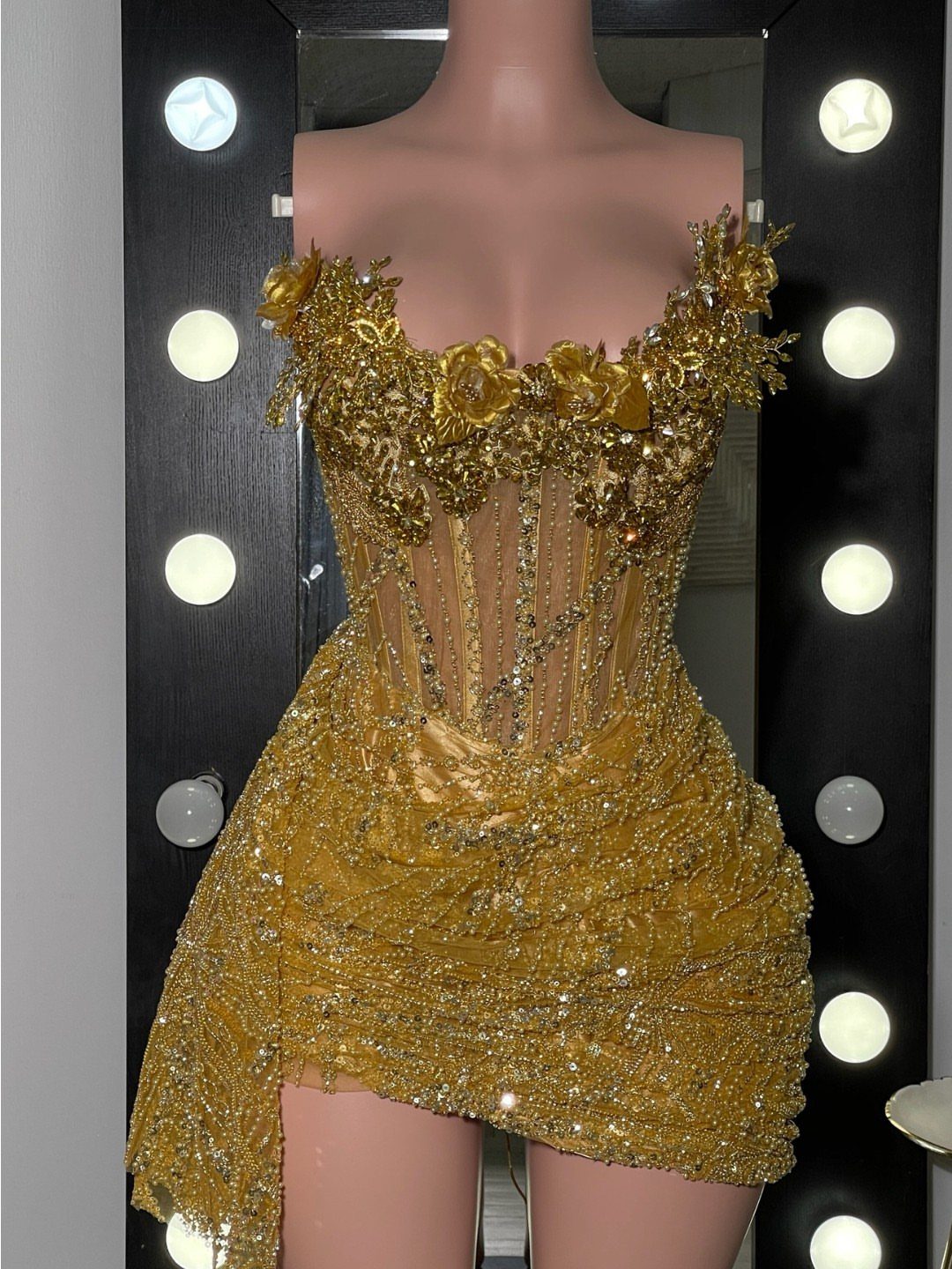 Gold sequined mini dress with corset bodice and floral details on a mannequin.