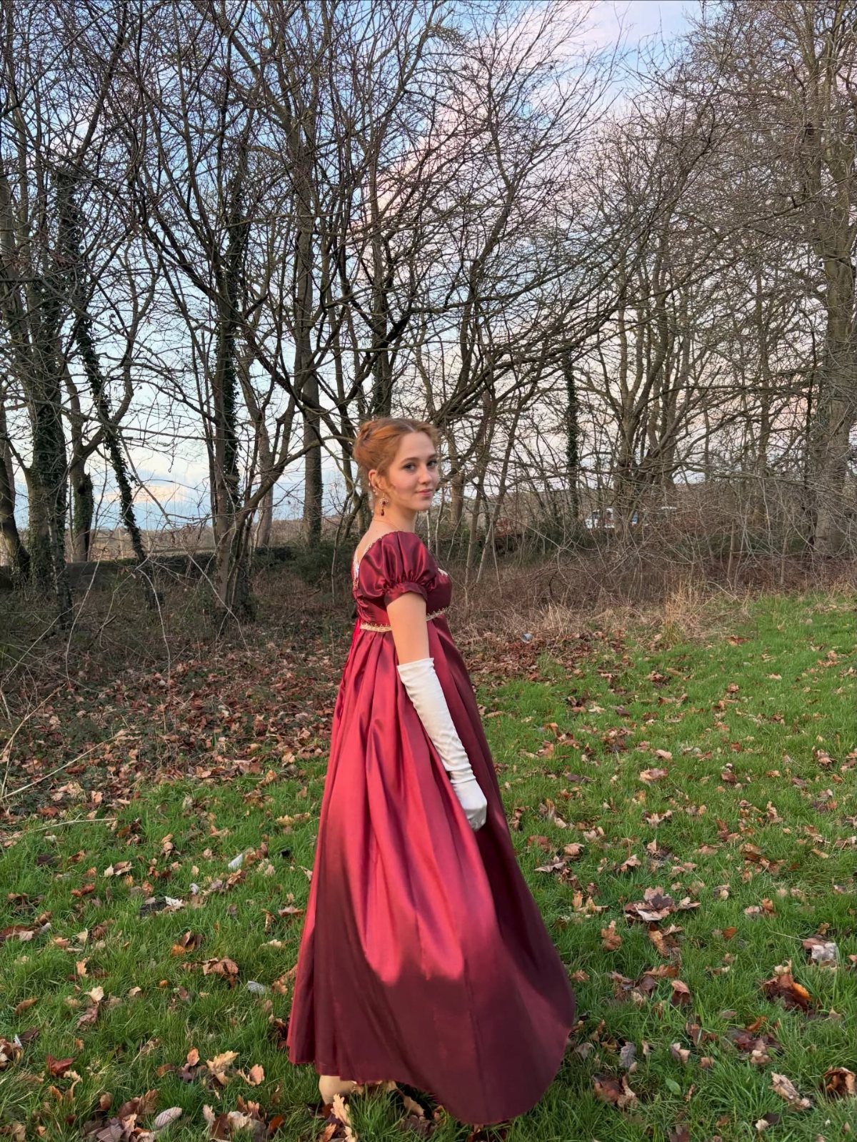 Woman in a burgundy satin regency gown and white gloves in a winter field