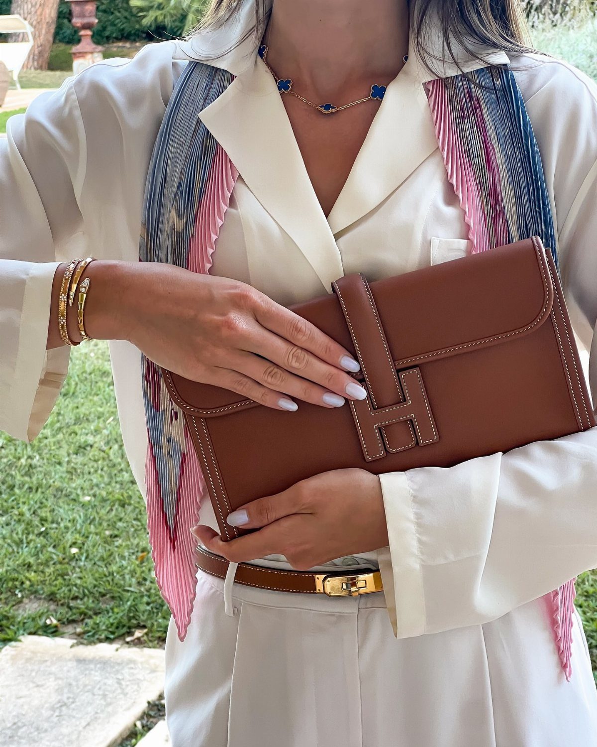 Woman holding a brown leather clutch with a colorful silk scarf and jewelry.