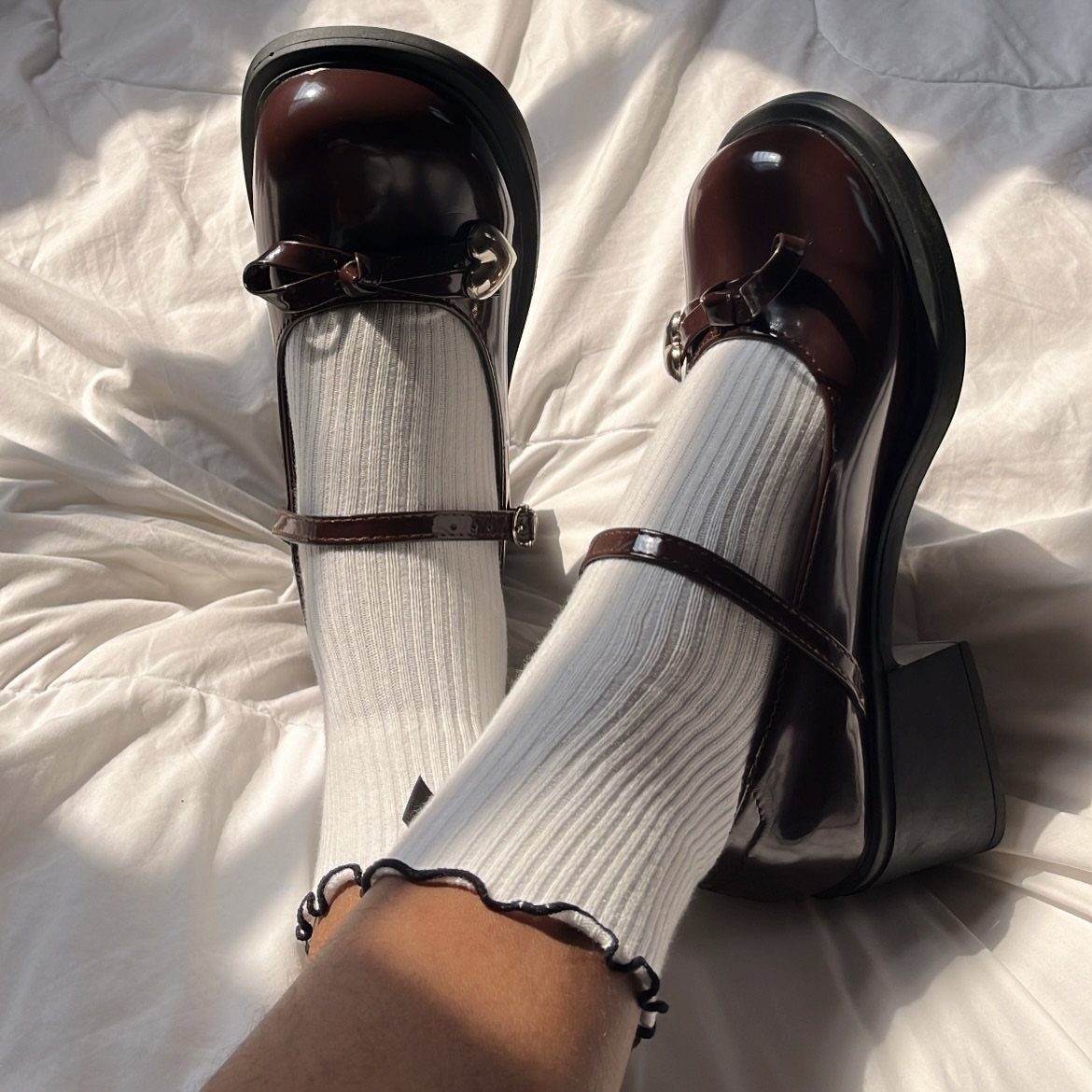 Burgundy patent leather Mary Jane shoes with white ruffled socks on white fabric.