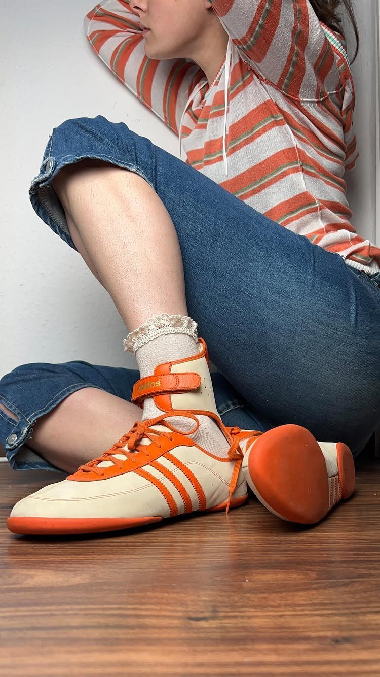 Cream sneakers with orange stripes and ankle straps worn with lace socks.