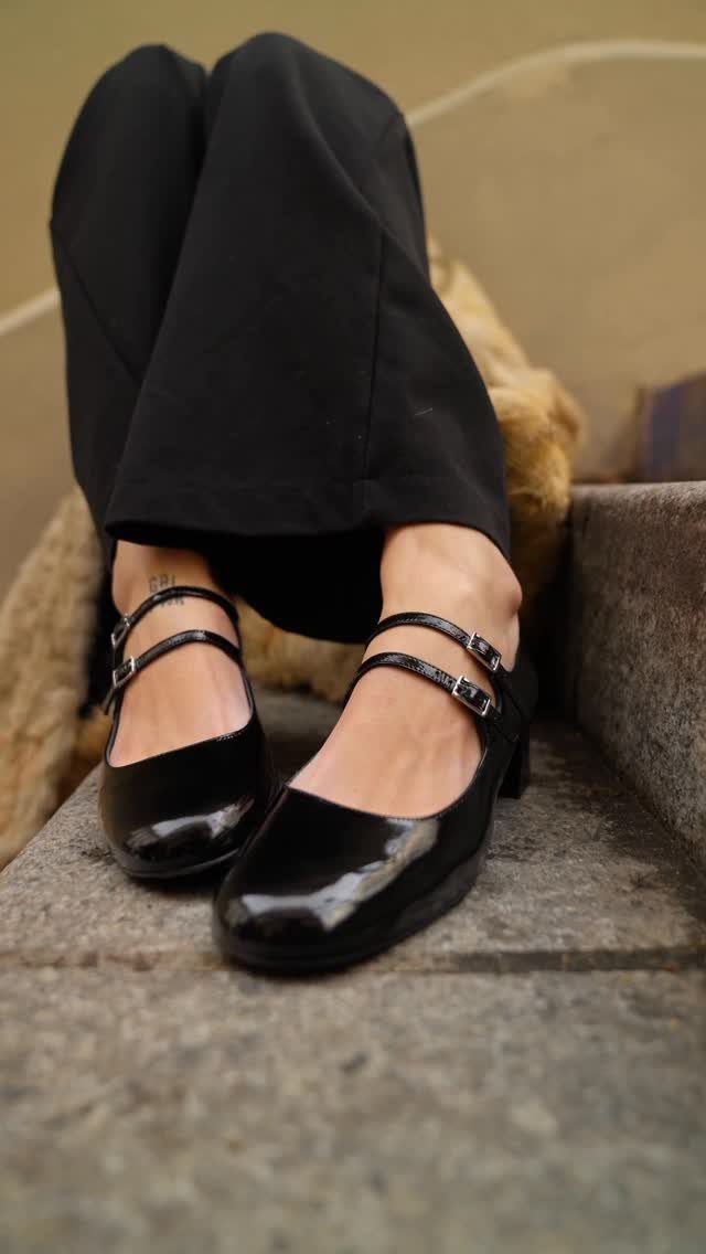 Black patent leather Mary Jane shoes with double straps and low block heels.