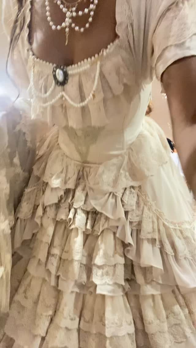 Cream-colored ruffled gown with lace details and pearl jewelry on a person