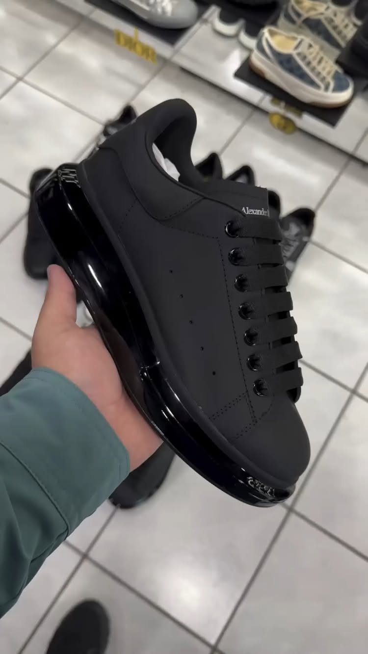 Black leather sneaker with a glossy sole held against a white tiled floor.