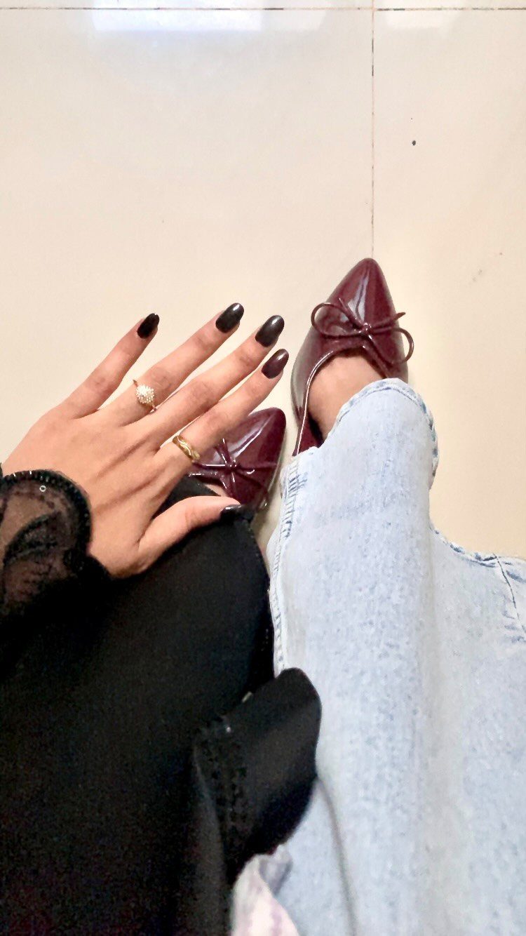 Burgundy pointed-toe flats with bows worn with light blue jeans on tiled floor