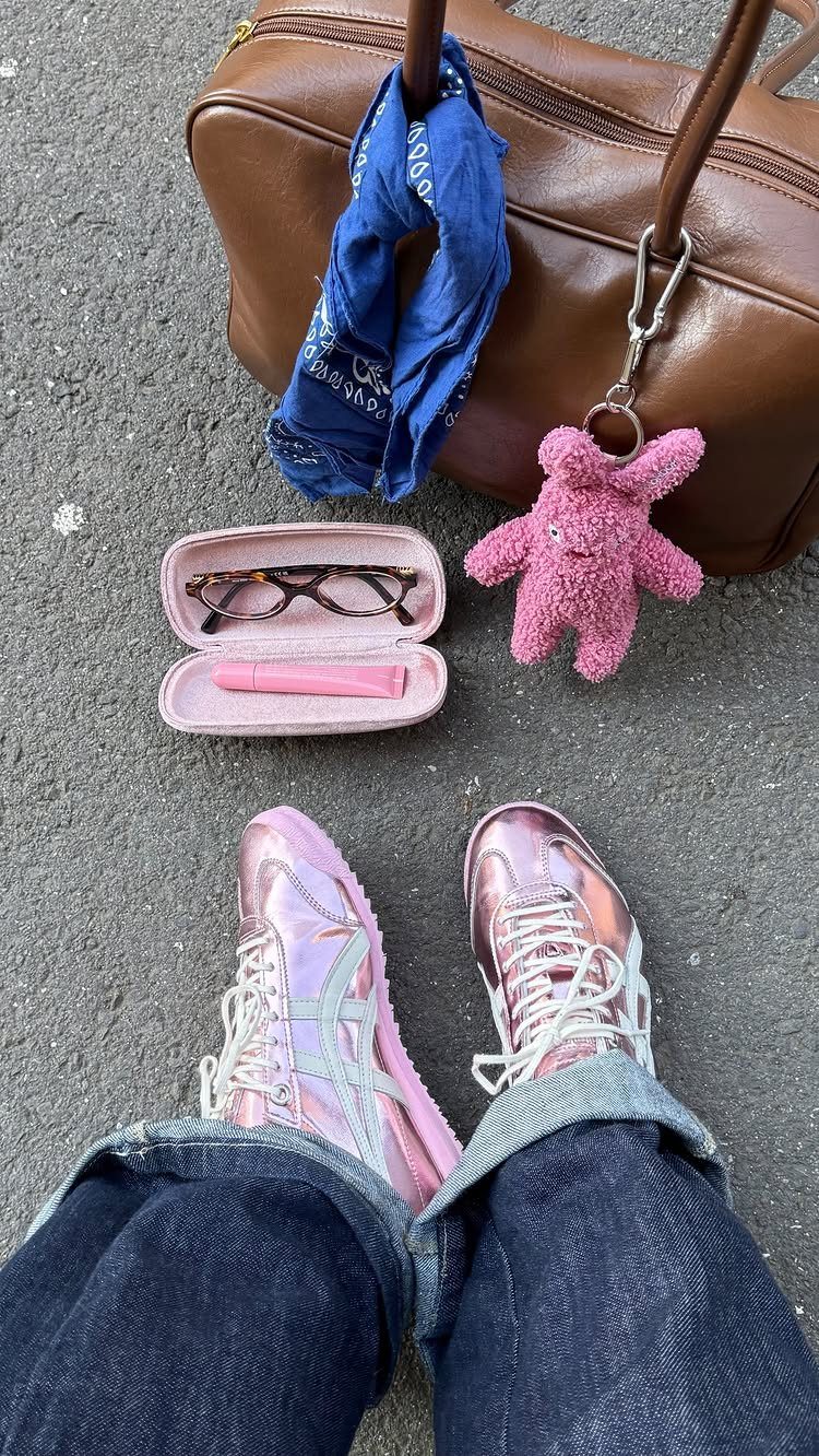 Iridescent metallic pink sneakers worn with dark blue jeans next to a brown handbag.
