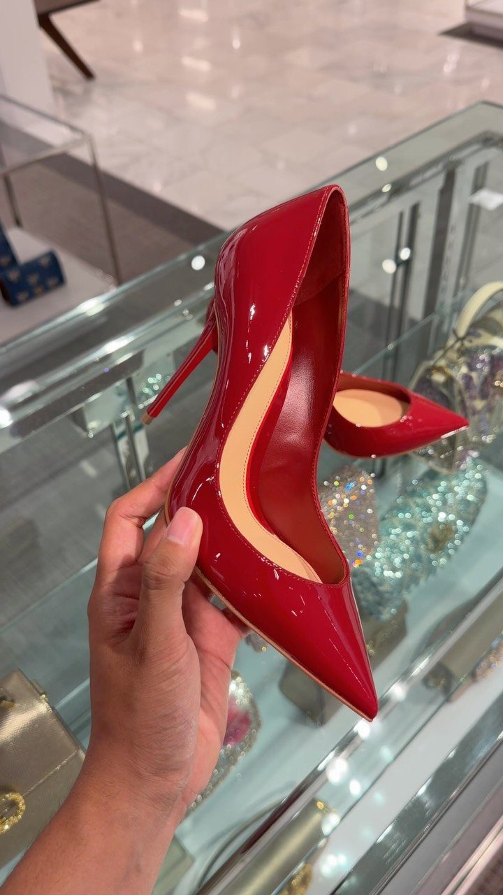 Glossy red patent leather high-heeled pumps held by a hand in a store.