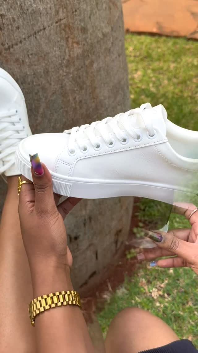 White leather lace-up sneaker held by hands with colorful nails against stone background