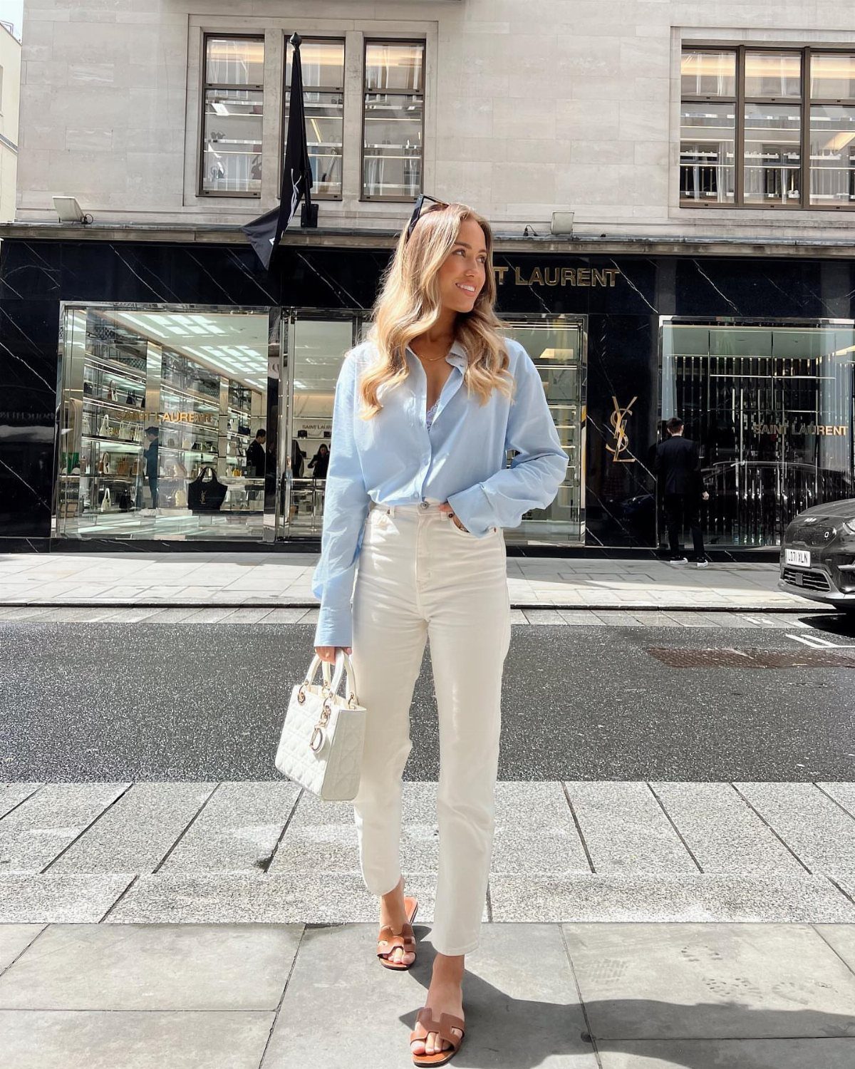 Woman in a light blue shirt and white trousers standing on a city street.