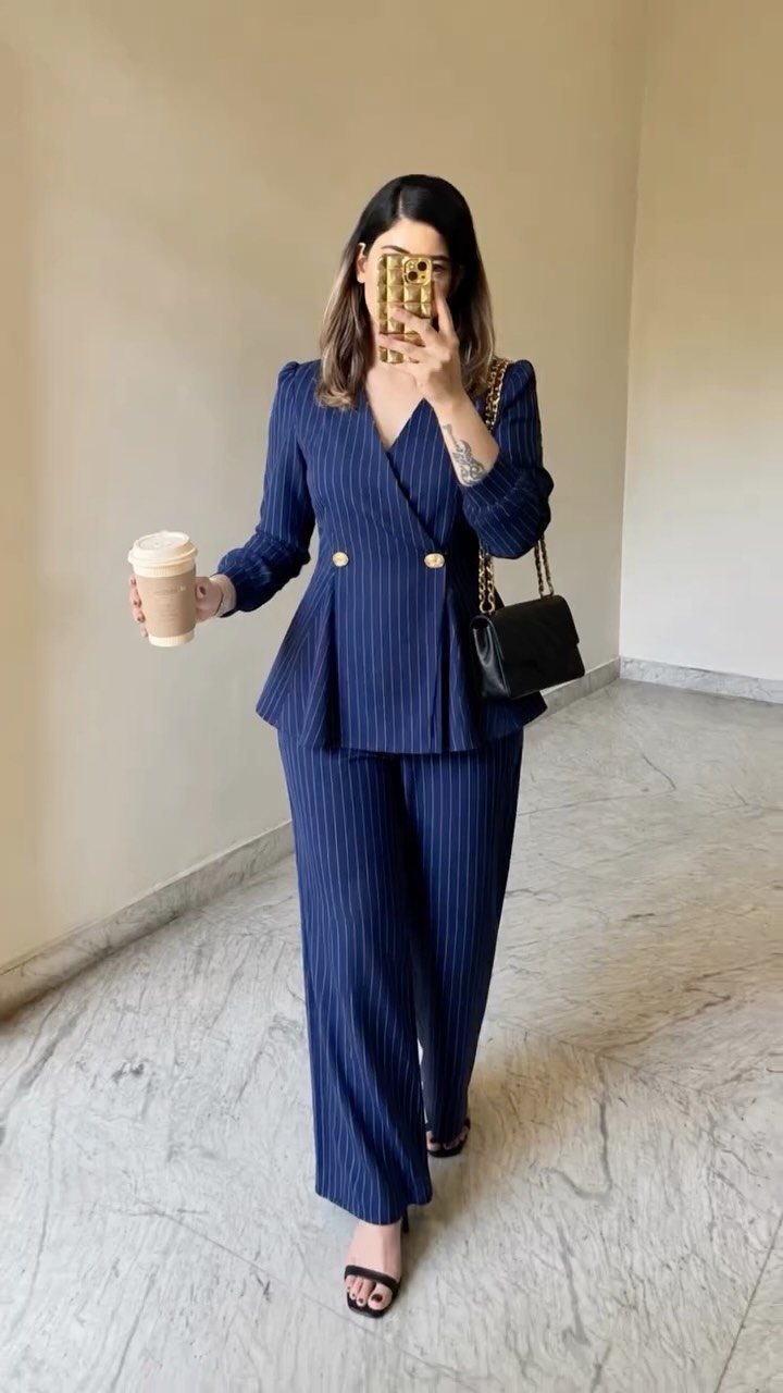 Woman in navy blue pinstripe suit holding coffee and a black handbag.