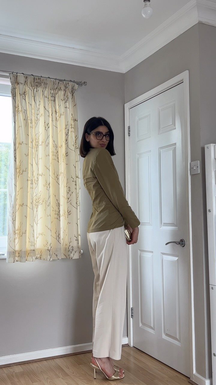 Woman wearing an olive green tailored blazer and cream wide-leg trousers in a room.