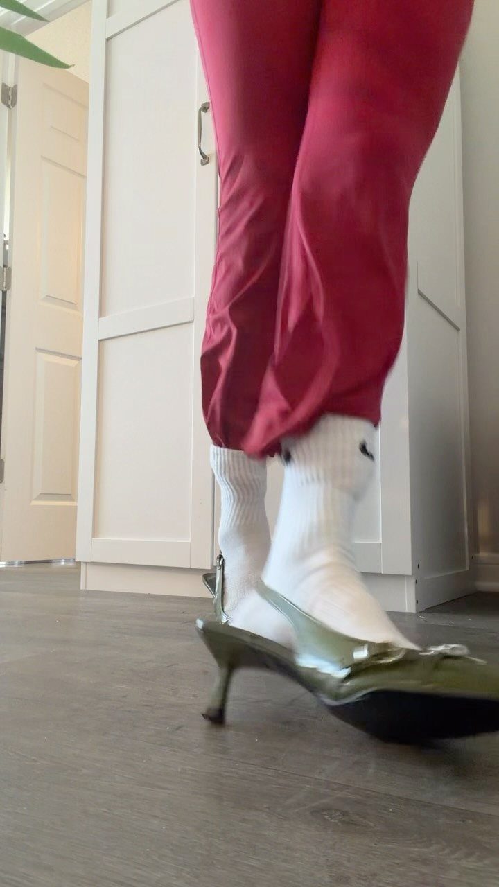 White crew socks with a logo worn with olive green pointed-toe pump heels.