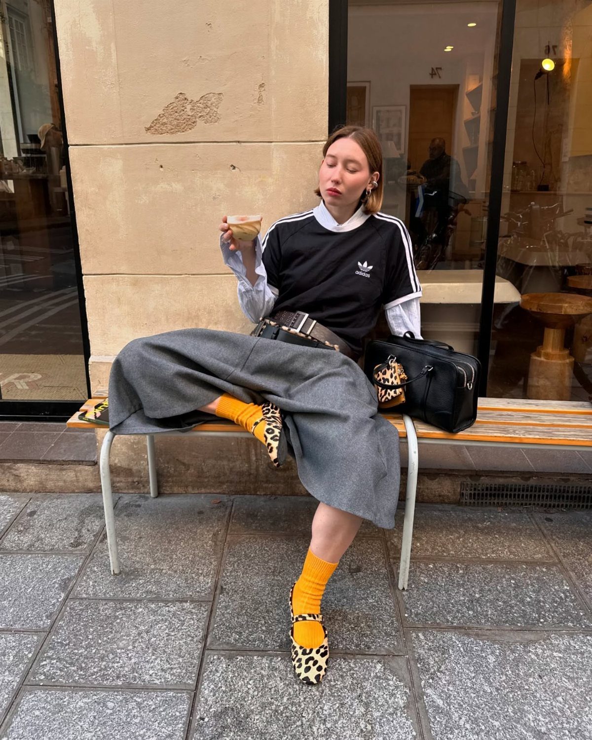 Woman wearing bright orange socks with leopard print pointed-toe pumps sitting on a bench
