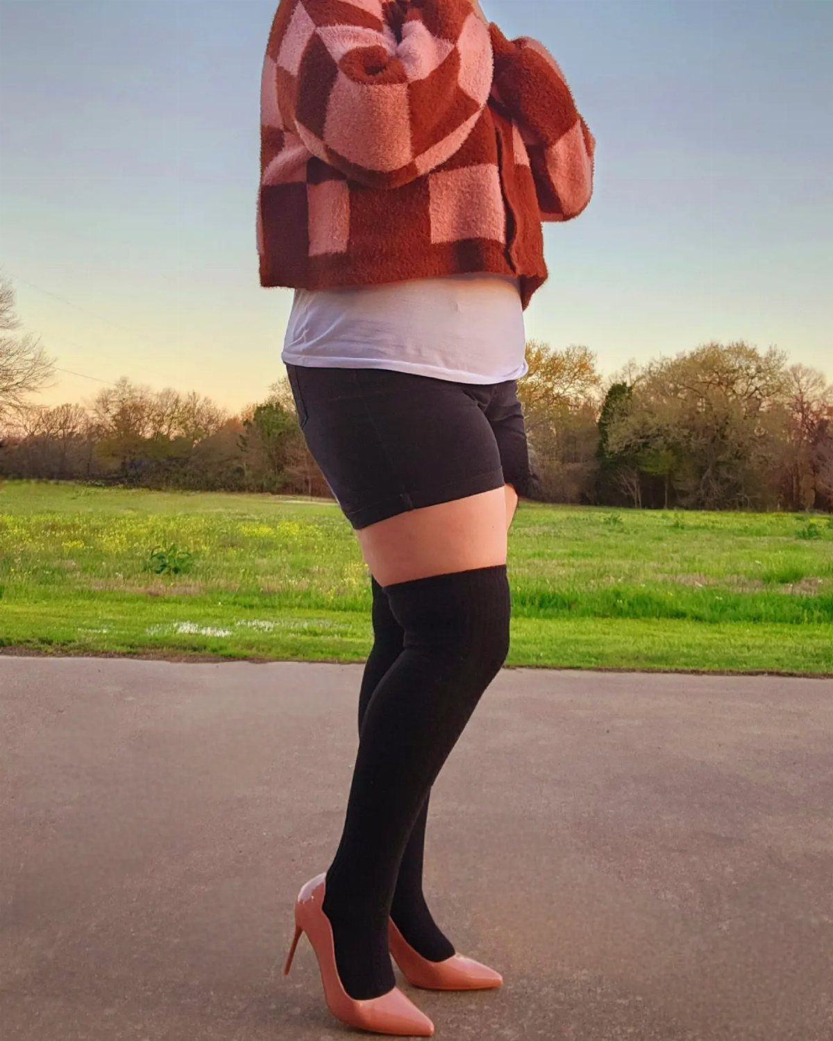 Person wearing black over-the-knee socks and nude pointed-toe pumps on a paved path.