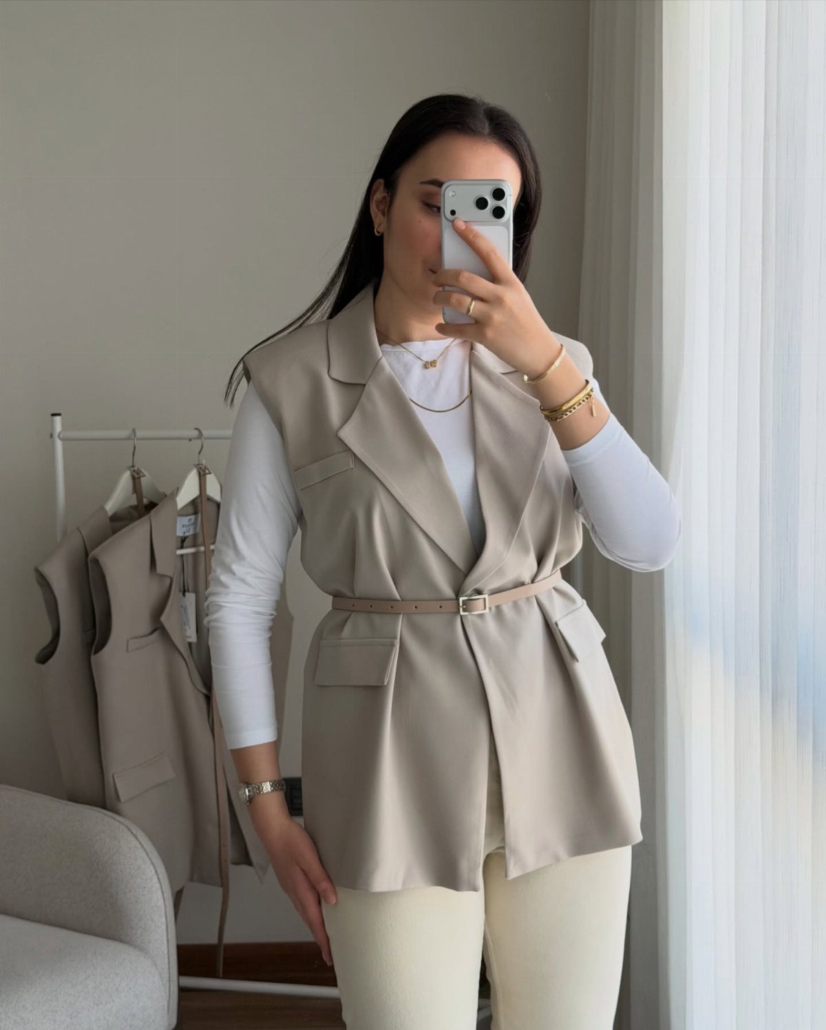 Woman wearing a beige sleeveless blazer vest with a belt and white trousers.
