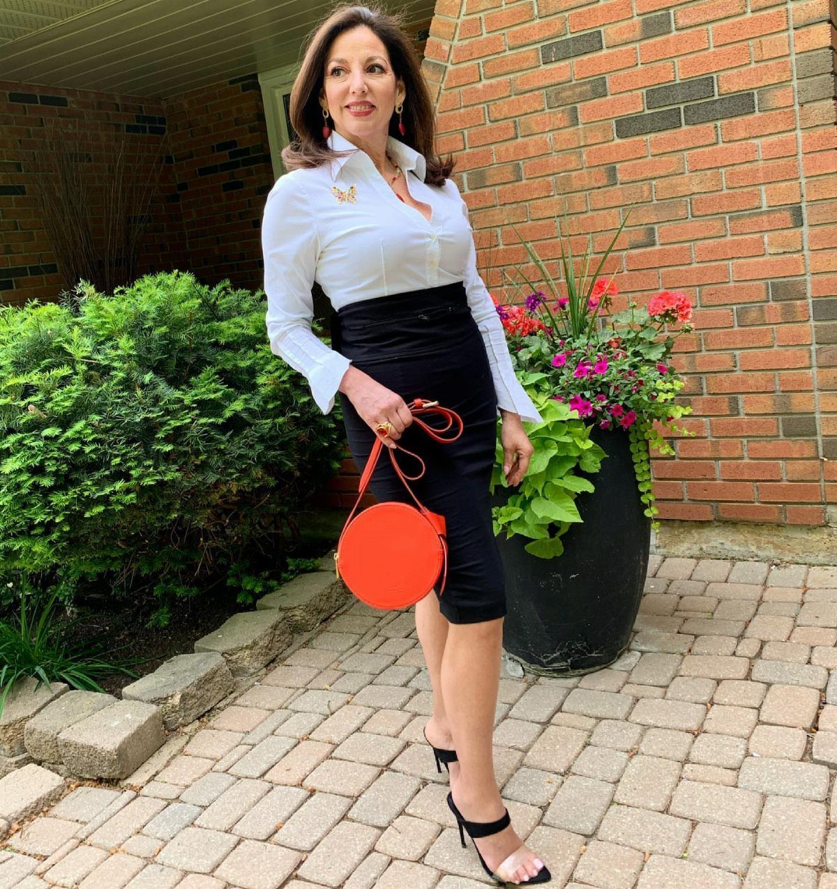Woman wearing a white button-down shirt and black pencil skirt with red handbag.