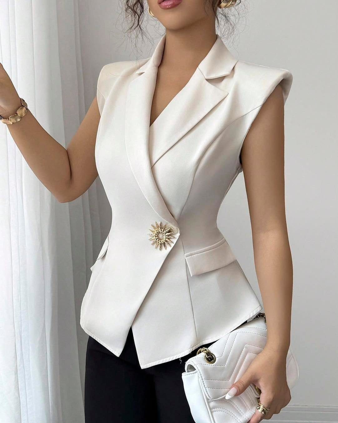 Woman wearing a cream sleeveless tailored blazer vest with a gold brooch.