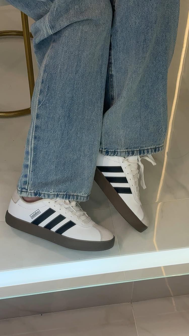 White Adidas tennis shoes with black stripes paired with wide-leg blue denim jeans.
