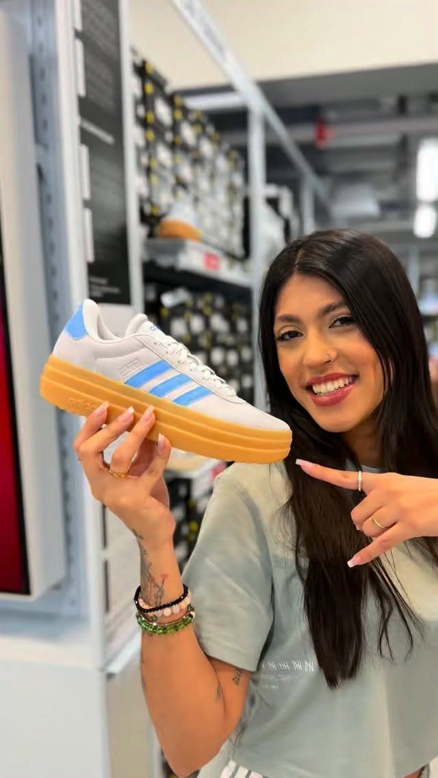 Woman holding a white Adidas VL Court platform sneaker with blue stripes.