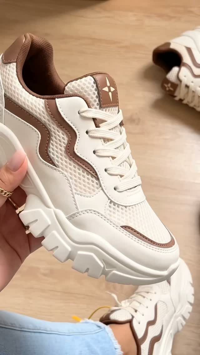 White chunky sneakers with brown accents and thick soles held by a person.