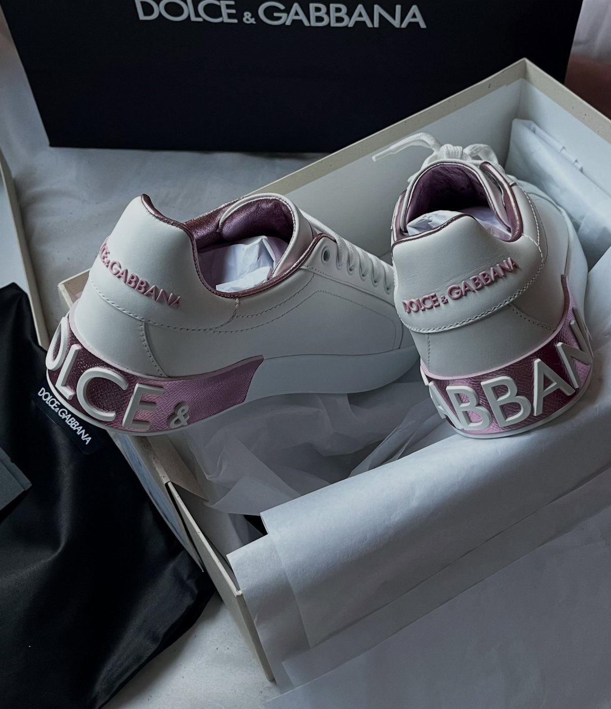 White Dolce & Gabbana sneakers with pink embossed lettering inside a white shoebox.
