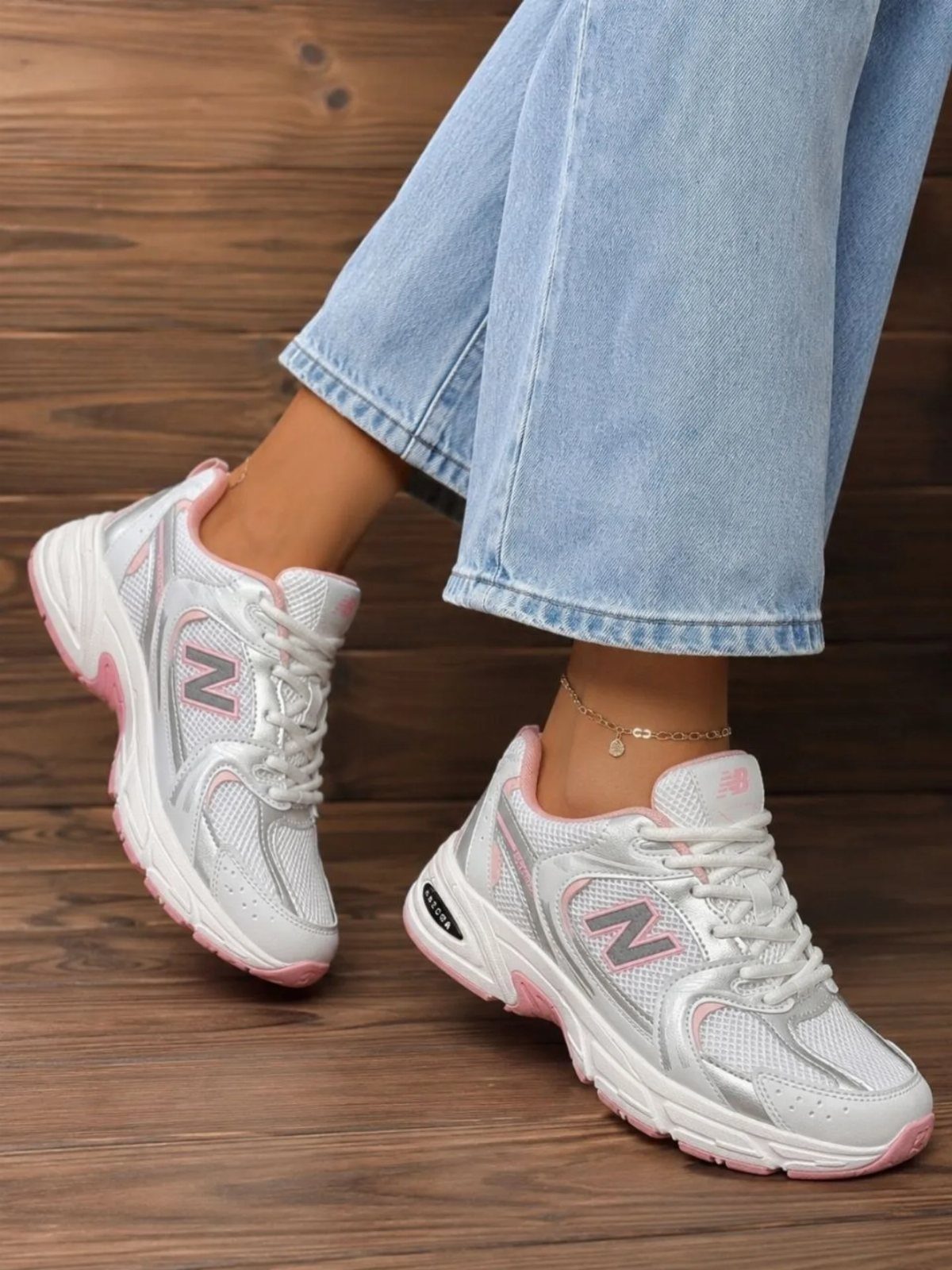 White New Balance sneakers with pink accents worn with light blue denim jeans.