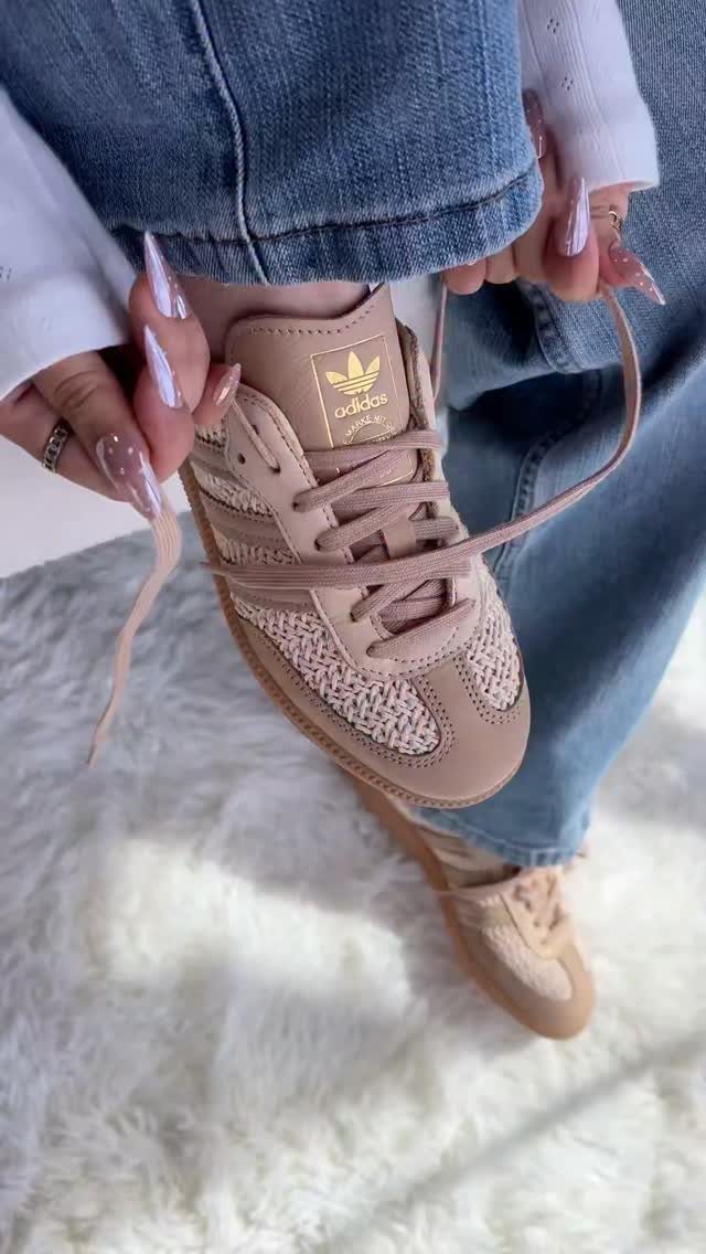 Pink Adidas sneakers worn with blue jeans on a white fluffy rug