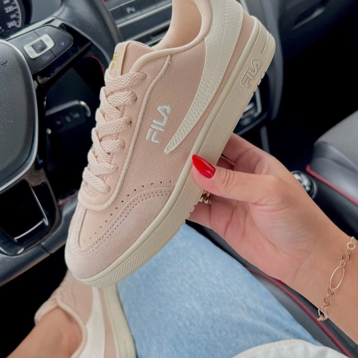 Light pink Fila sneaker held by a hand inside a car interior.