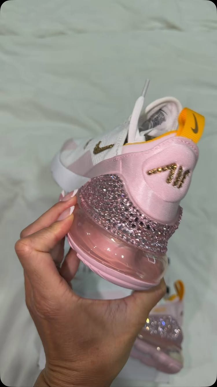 Pink and white rhinestone embellished Nike sneakers held by a hand against white fabric