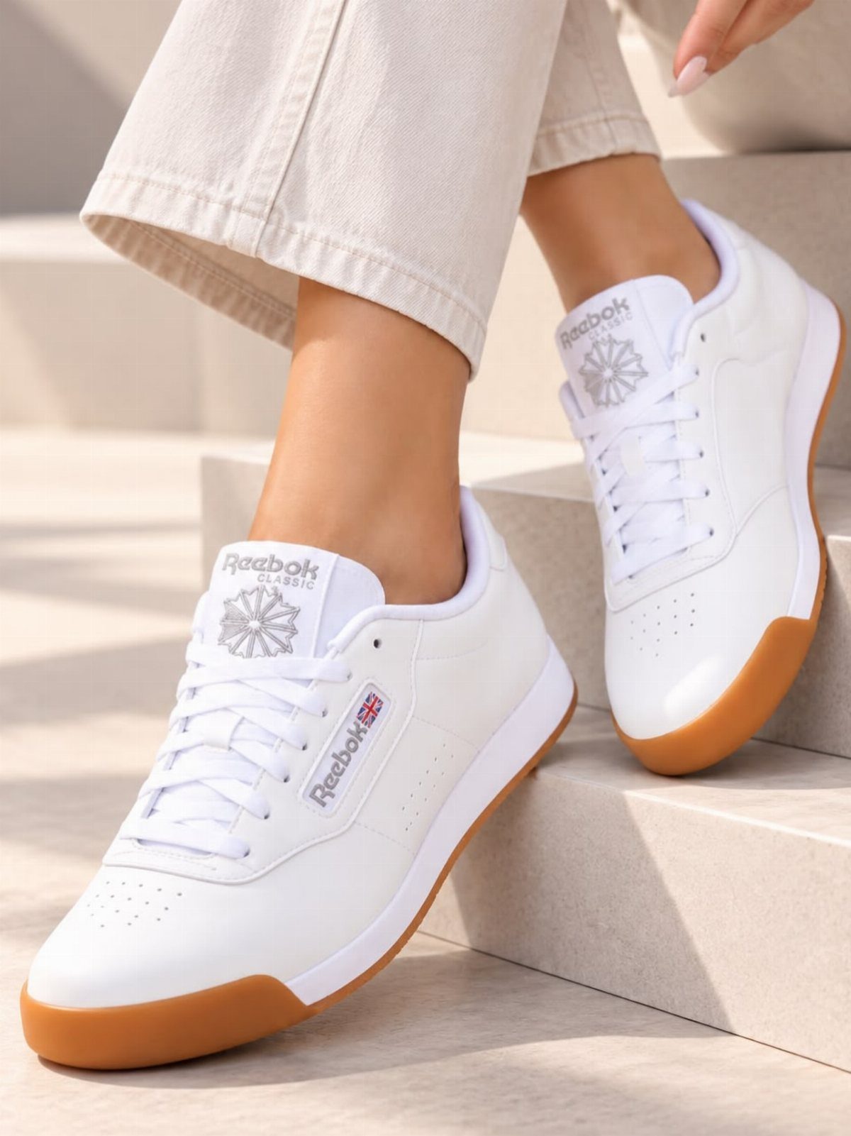 White Reebok sneakers with gum soles worn with beige trousers on stone steps.