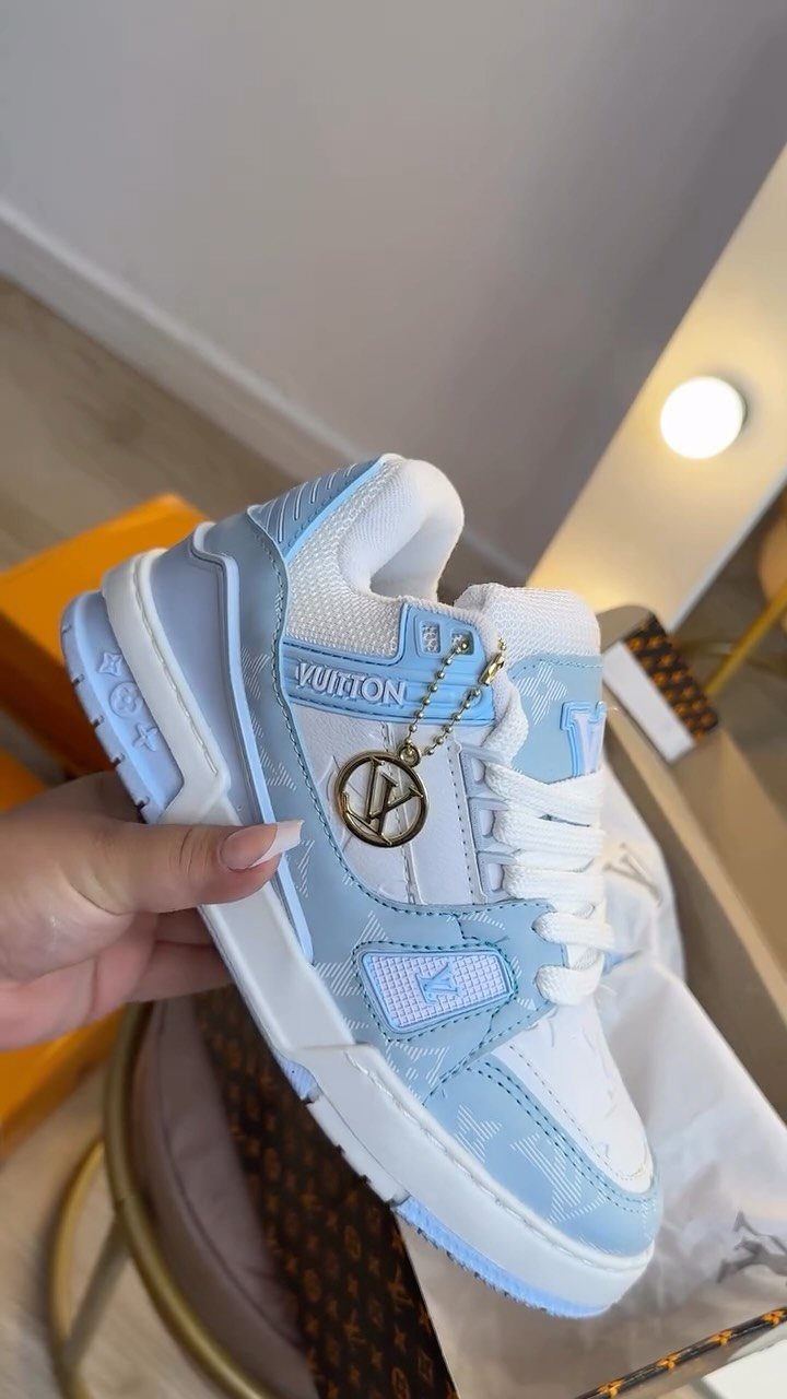 White and light blue luxury sneaker with gold LV charm held by hand