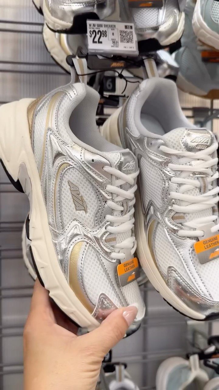 White and silver metallic sneakers with gold accents held in a retail store.