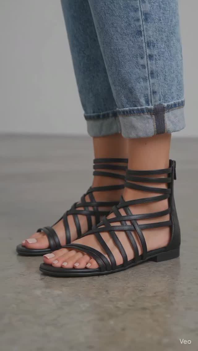 Black flat gladiator sandals with criss-cross straps worn with cuffed blue jeans.